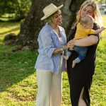 nő kisbabával, mellette idősebb nő kalapban, a kisbabát simogatja