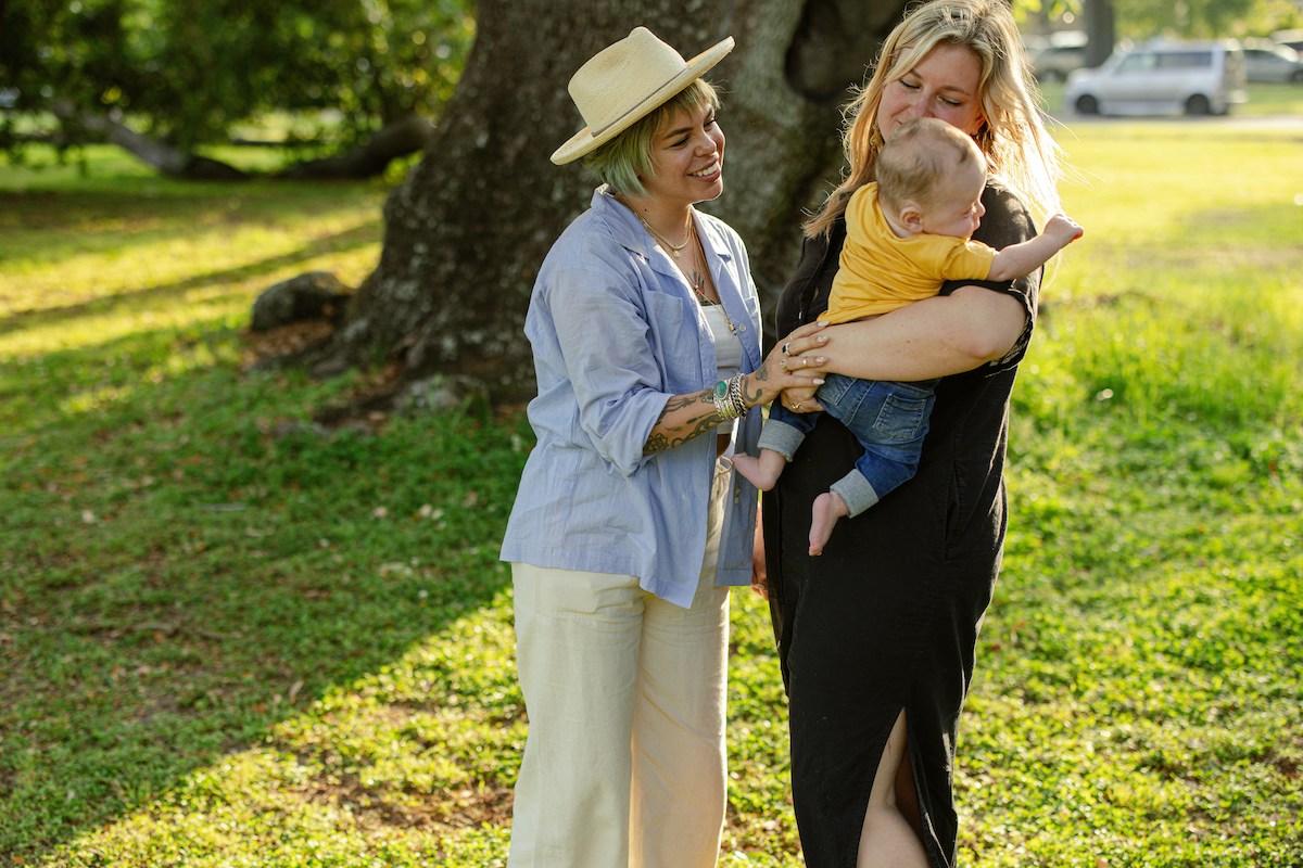 nő kisbabával, mellette idősebb nő kalapban, a kisbabát simogatja