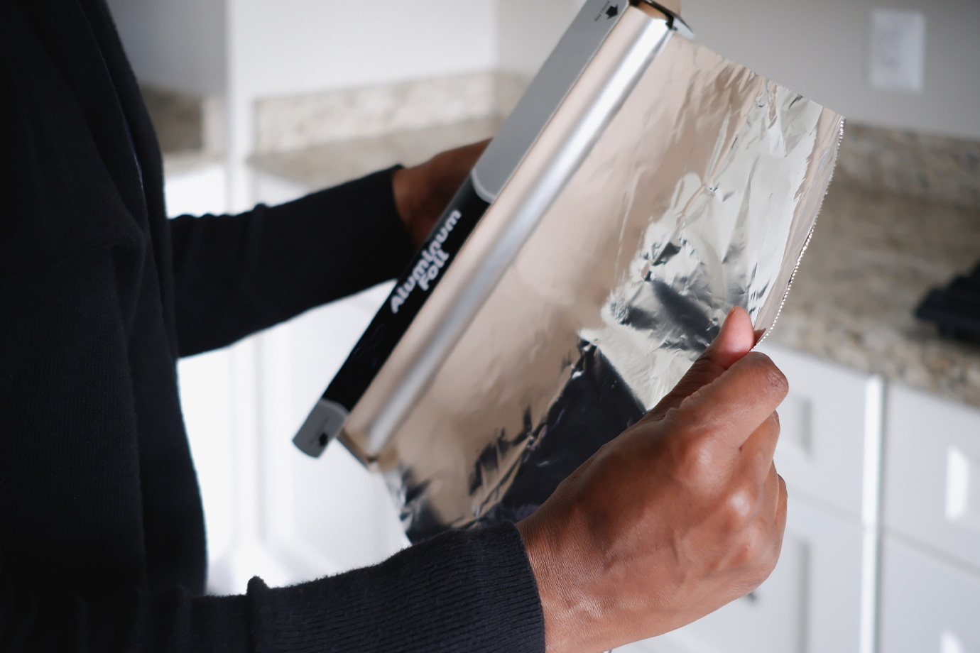 Egy fekete ruhás nő alufóliát tép le a konyhában