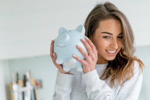 Boldog fiatal nő pénzt megrázza a fehér malacperselyt