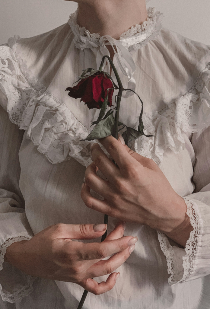 Jane Austen-korabeli fehér felsőrészben nő törzse nyaktól lefelé, hervadt vörös rózsát tart a kezében