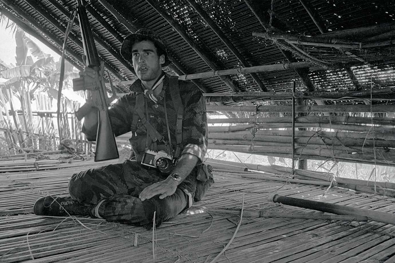 Sean Flynn egy gépfegyverrel a kezében ücsörög