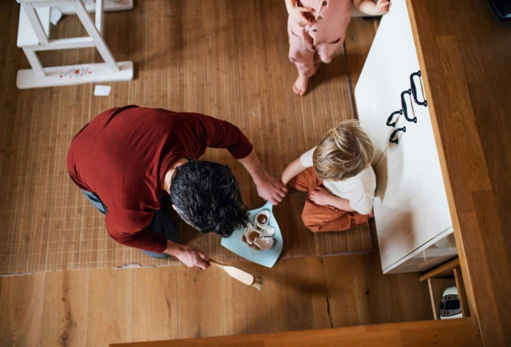 Apuka söpri fel az összetört csészét kék lapátra, mellette térdel a gyerek, felülnézetből