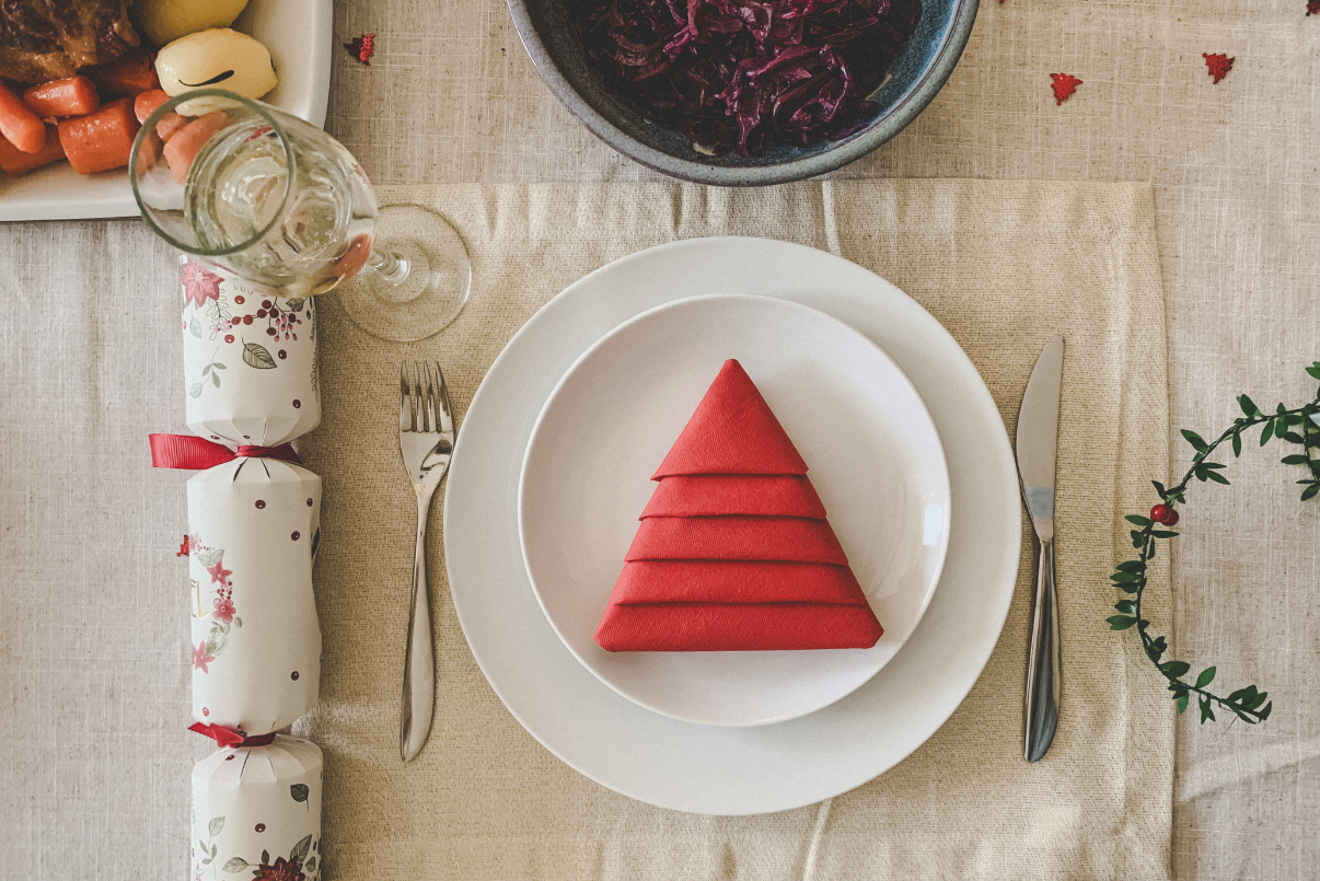 karácsonyi asztal megterítve, a tányéron piros szalvéta karácsonyfának hajtogatva