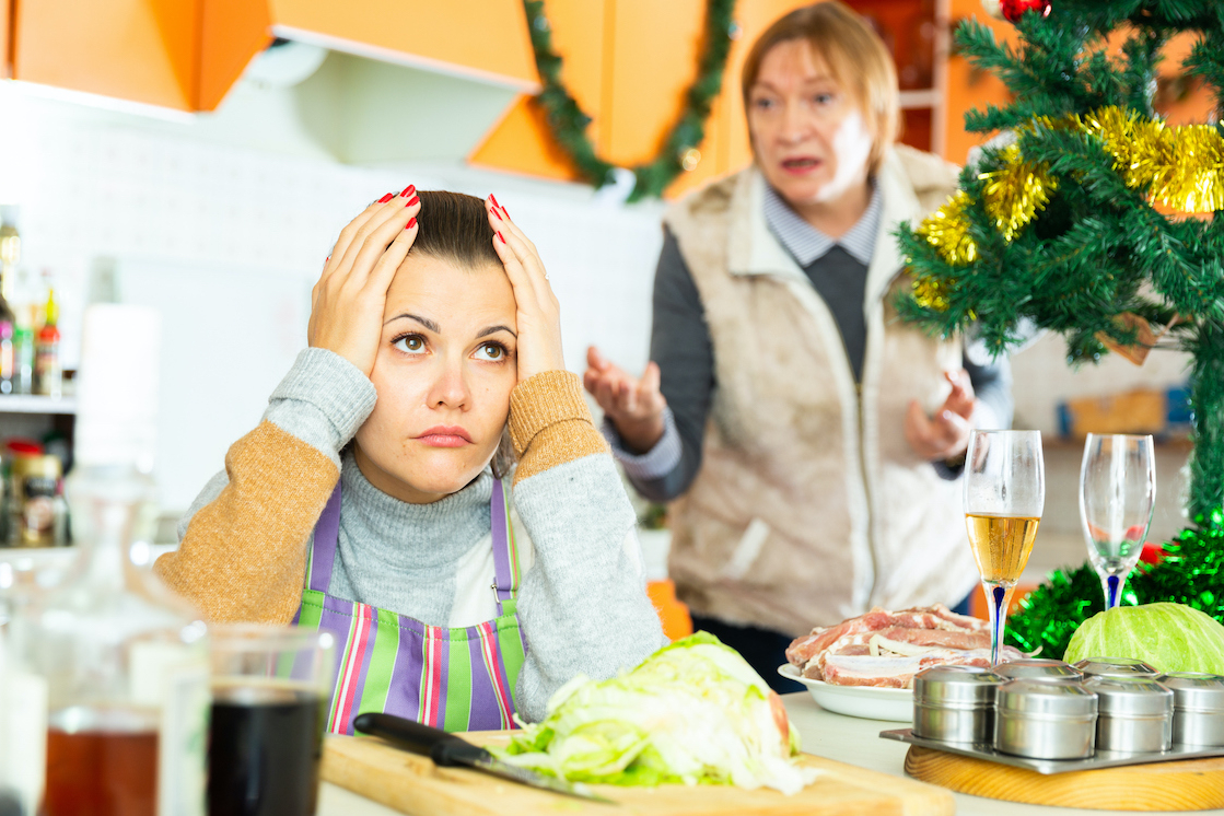 karácsonyi konyhaasztalnál ülő nő a fejét fogja, a háttérben idősebb nő magyaráz