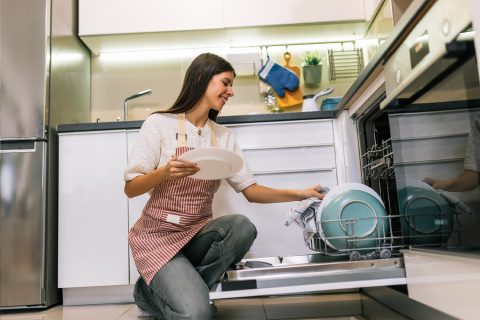Fiatal nő mosolyogva beteszi a tányért a mosogatógépbe