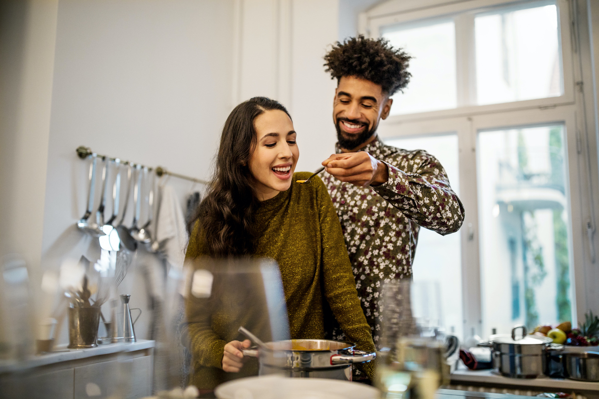 Szakállas fiatal férfi levest kanalaz fiatal nő szájába a konyhában