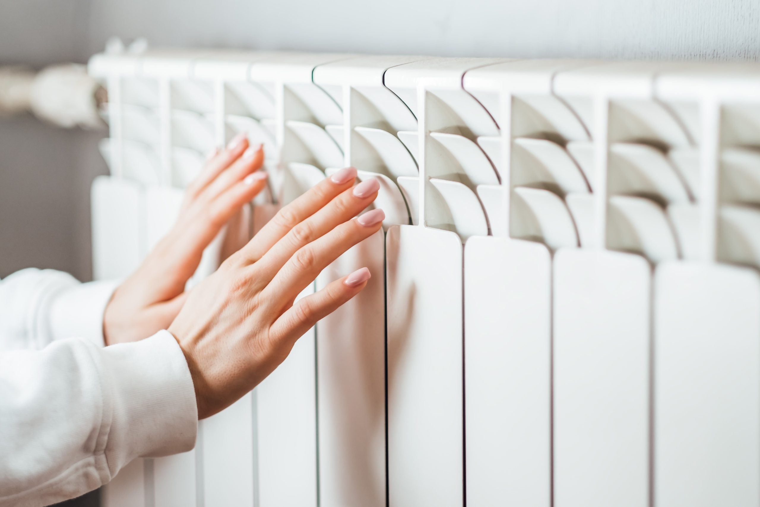 Egy nő melegíti a hideg kezet a radiátornál