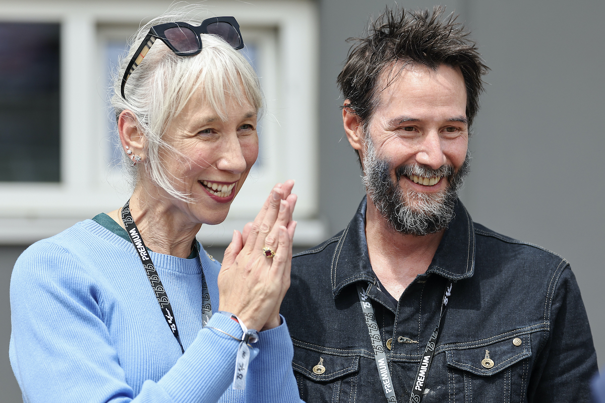 Keanu Reeves fekete dzsekiben, szakállal és Alexandra Grant világoskékben, napszemüveggel a fején