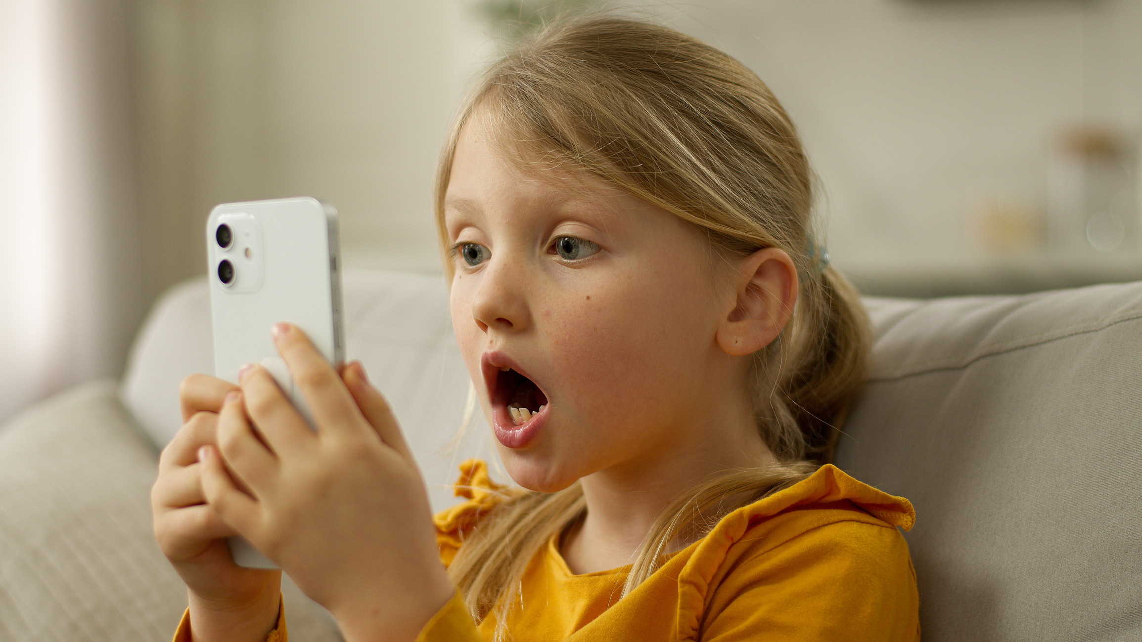 Gyerek mobiltelefont néz a kanapén