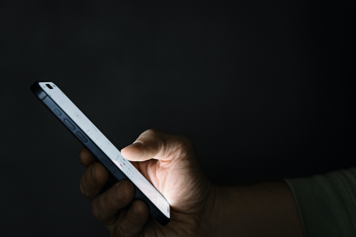 sötétben mobiltelefont tartó kéz