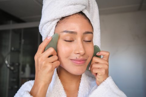 Fiatal nő gua sha arcmasszázst végez a fürdőszobában