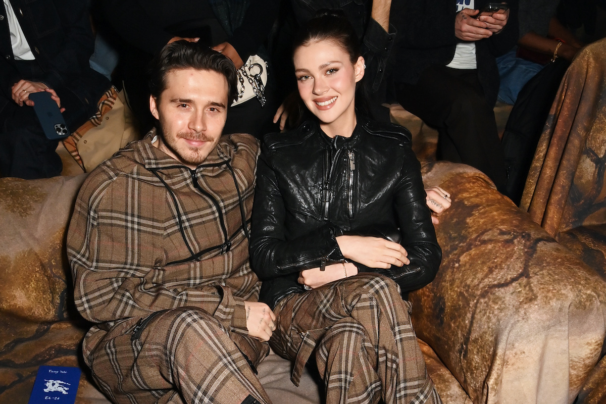 Brooklyn Beckham kockás szettben és Nicola Peltz kockás nadrágban és fekete bőrdzsekiben ülnek a Burberry 2025 téli bemutatóján a London Fashion Weeken 2025. február 24-én.