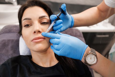 Kék kesztyűt viselő kozmetikus vagy doktor Botox-injekciót ad be egy női páciens ajkaiba.