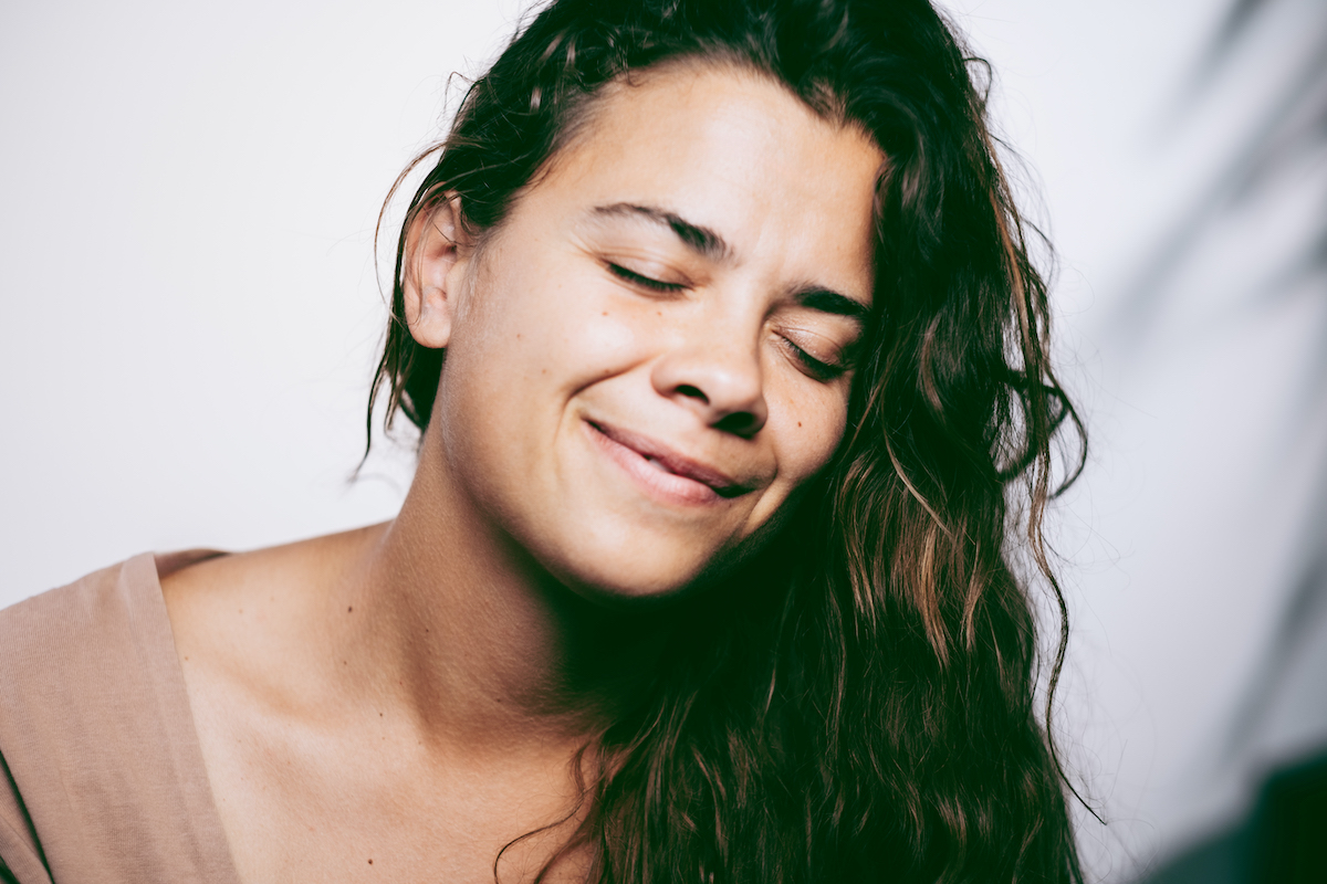 fiatal hosszú barna hajú nő csukott szemmel mosolyog