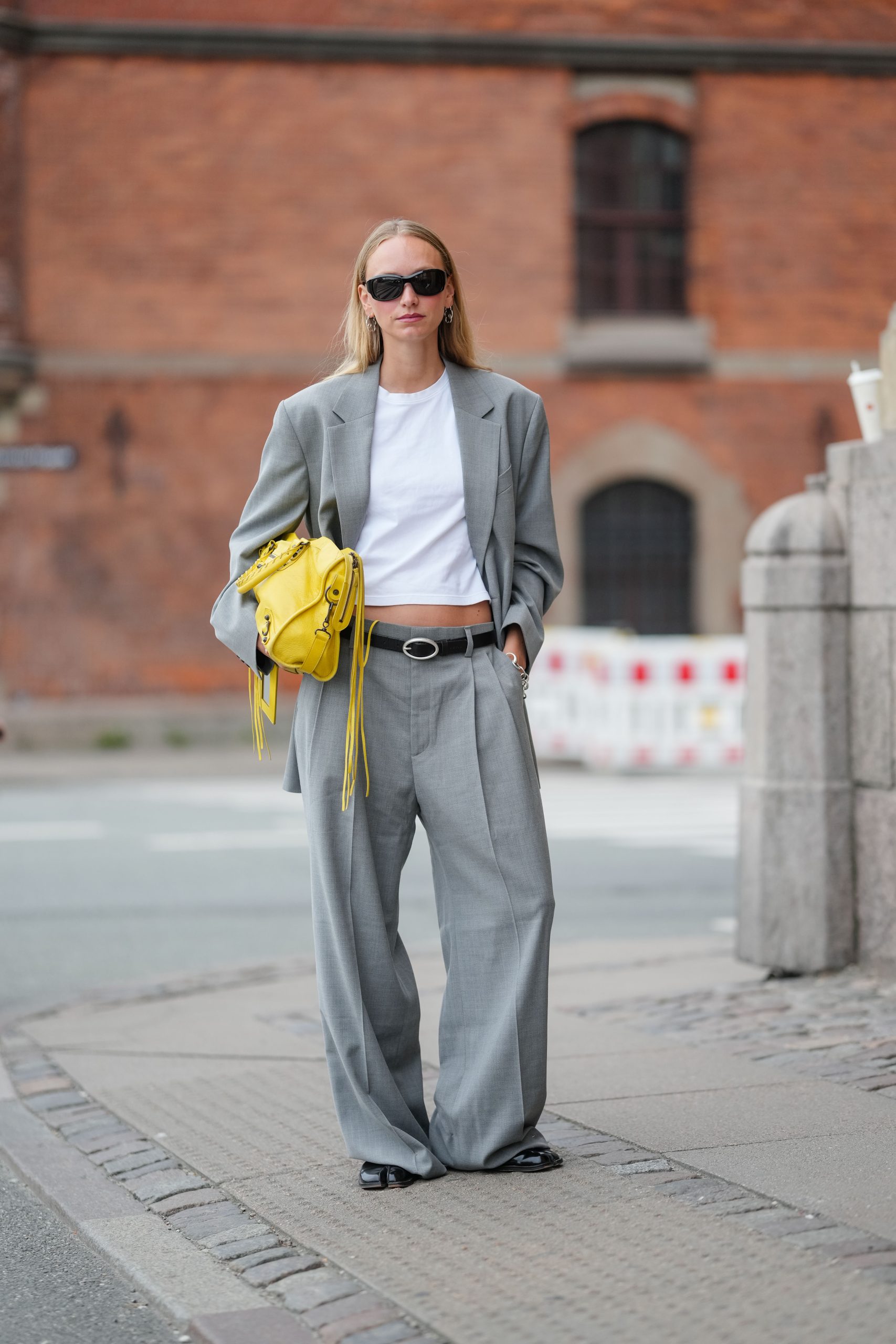 A vendég világosszürke, testre szabott blézert visel fehér, rövid póló felett., és elegáns nadrágot.