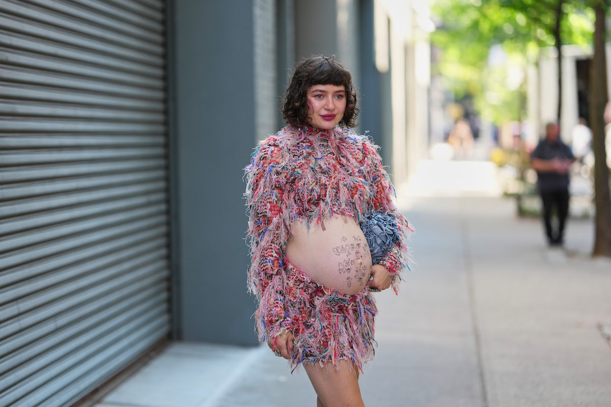 frufrutrend-2026-5-divatos-fazon-hajvagashoz | Marie Claire Fiatal nő rövid, sötétbarna, göndör bob frizurát visel egyenes frufruval; mindkét kezén több ezüstgyűrűt; kerek, fodros, kékesszürke anyagból készült válltáska ezüst láncpánttal; összeillő, kétrészes, sokszínű, bozontos rojtos kötött szett, magas nyakú, hosszú ujjú, rövid felső és hozzá illő miniszoknya. A szett rózsaszín, piros, kék és krémszínű, kevert fonalakból készült, nyers, rojtos szegélyekkel. A Zankov üzlet előtt, a New York-i Divathéten, 2025.