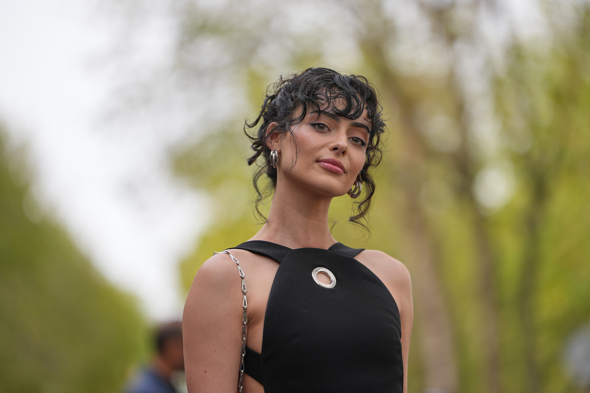 frufrutrend-2026-5-divatos-fazon-hajvagashoz | Marie Claire Aubri Ibrag sötétbarna, göndör feltűzött frizurát visel rövid, göndör frufruval; ezüst karika fülbevalókat; ujjatlan fekete felsőt aszimmetrikus peplum résszel, a nyakkivágásnál kerek ezüst fémkarikával és oldalsó kivágásokkal. Rabanne Párizsi Divathét, 2025.