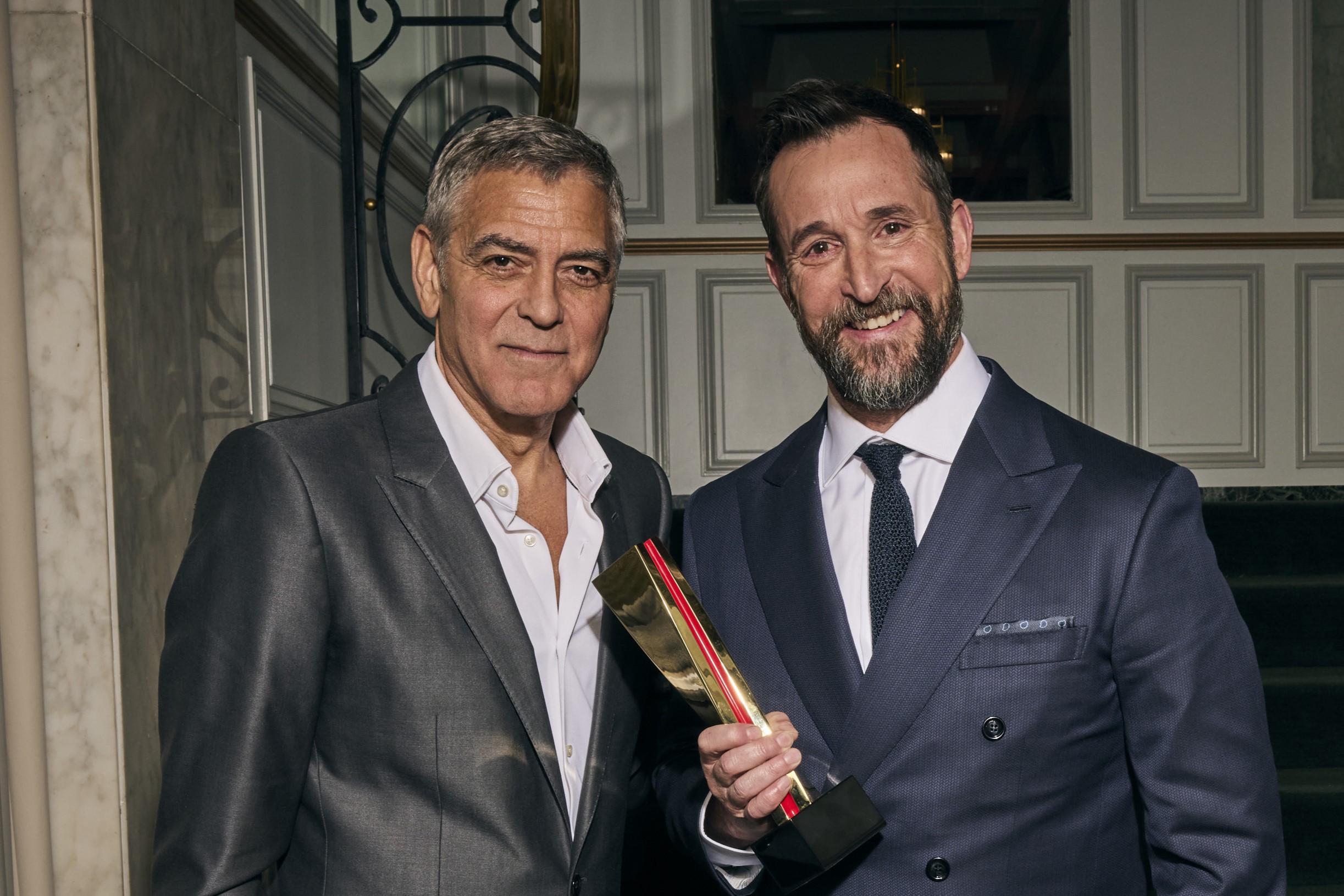 George Clooney és Noah Wyle öltönyben, Wyle kezében díj, a 2026-os Annual Movies for Grownups Awards with AARP díjátadón 2026 január 10-én.