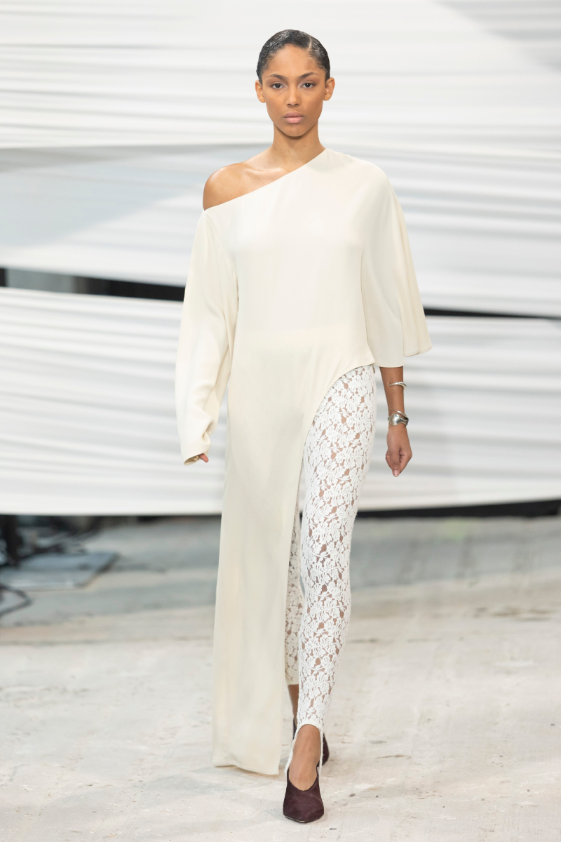 Barna hajú modell a Herskind 2026-os őszi–téli bemutatóján fehér tunikában és fehér csipkenadrágban