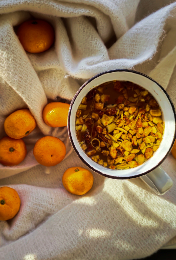 Meleg hangulatú képen mandarinok egy csésze gyógynövényes tea mellett felülnézetből, alattuk konyharuha