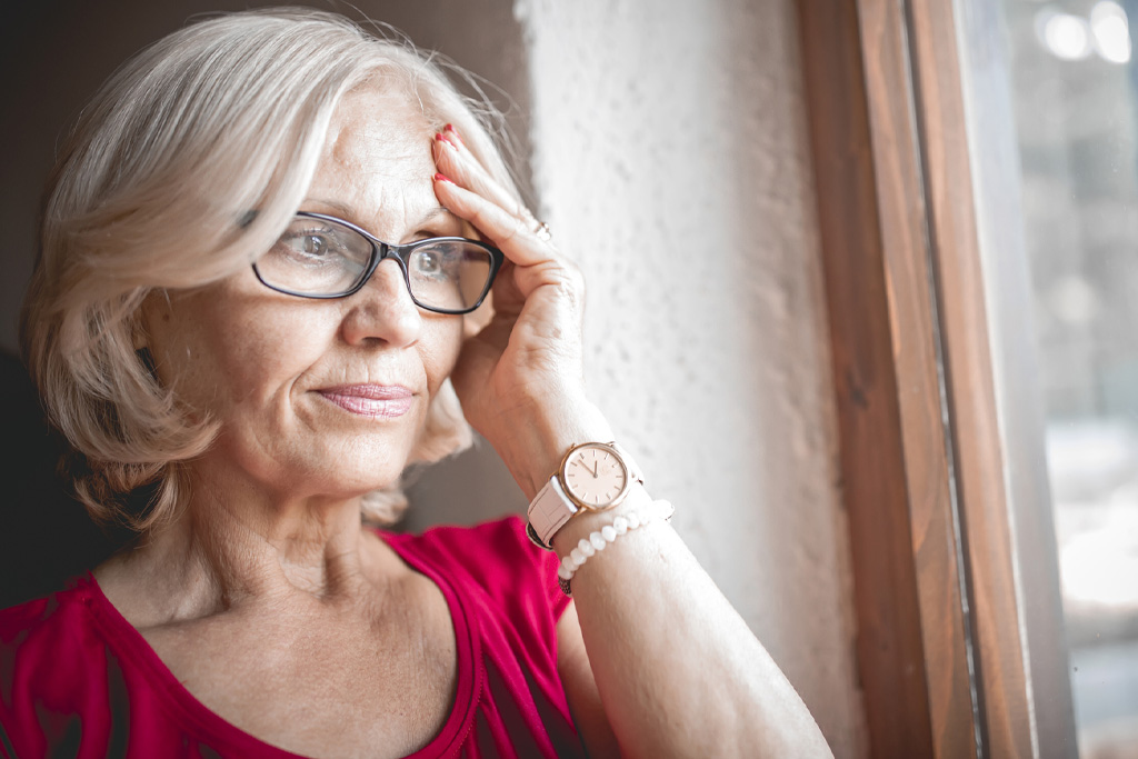 Egy idős szemüveges nő kétségbeesetten fogja a fejét