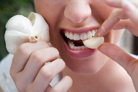 Egy nő szájába vesz egy gerezd fokhagymát, miközben a kezében is fokhagymát tart