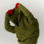 Nő zöld cipzáras nyakú kötött téli pulóvert húz át a fején piros kesztyűben