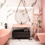 Modern fürdőszoba fehér márvány fallal, kör alakú, keret nélküli tükörrel, fekete mosdóval, amin rózsaszín mosdókagyló van, rózsaszín kád és vécé