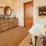 Otthonos fürdőszoba fa ajtóval, mosdópulttal, fehér káddal, barnás szőnyeggel