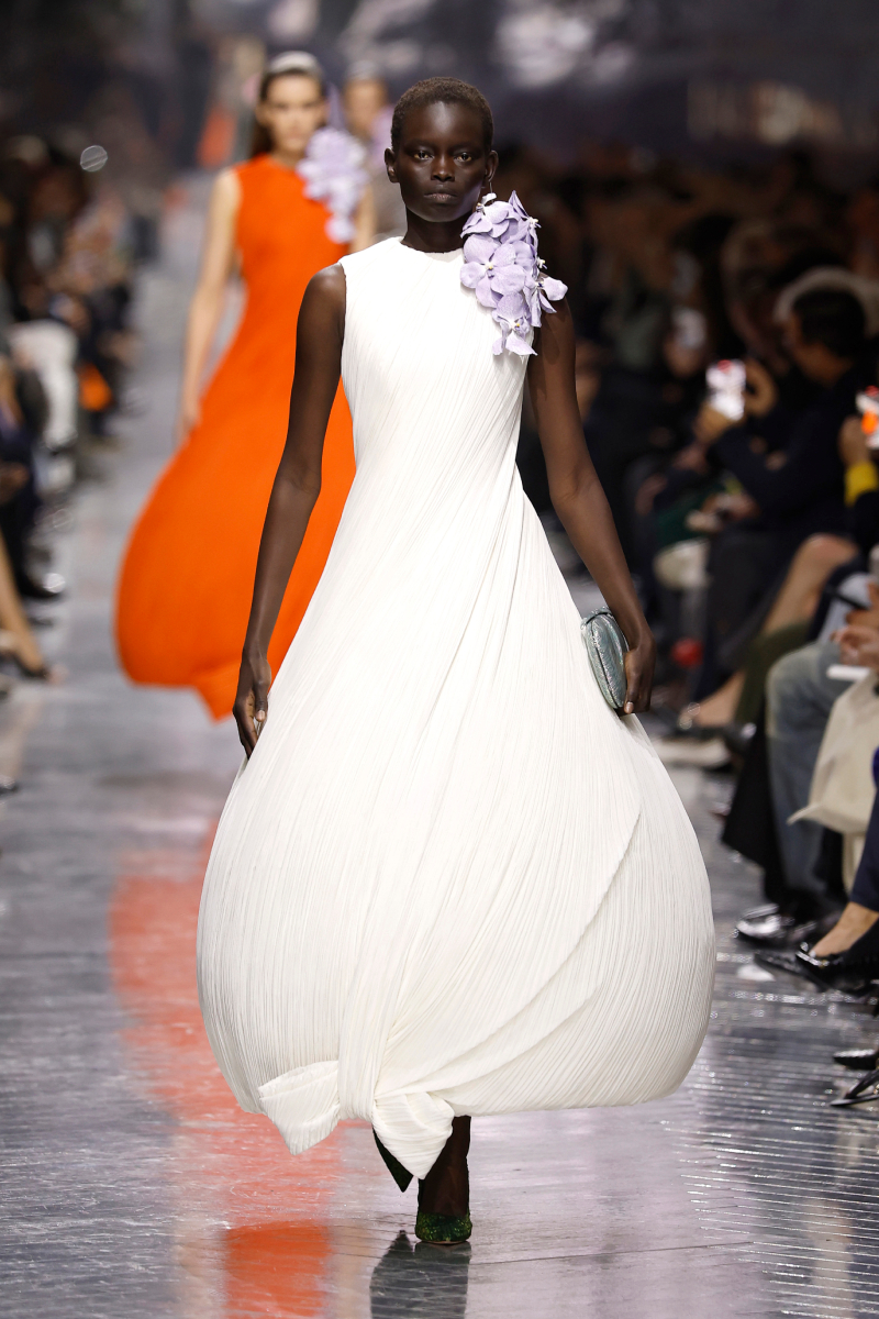 Fekete bőrű modell a Christian Dior 2026-os tavaszi–nyári haute couture bemutatóján fehér ruhában, vállán orchidea
