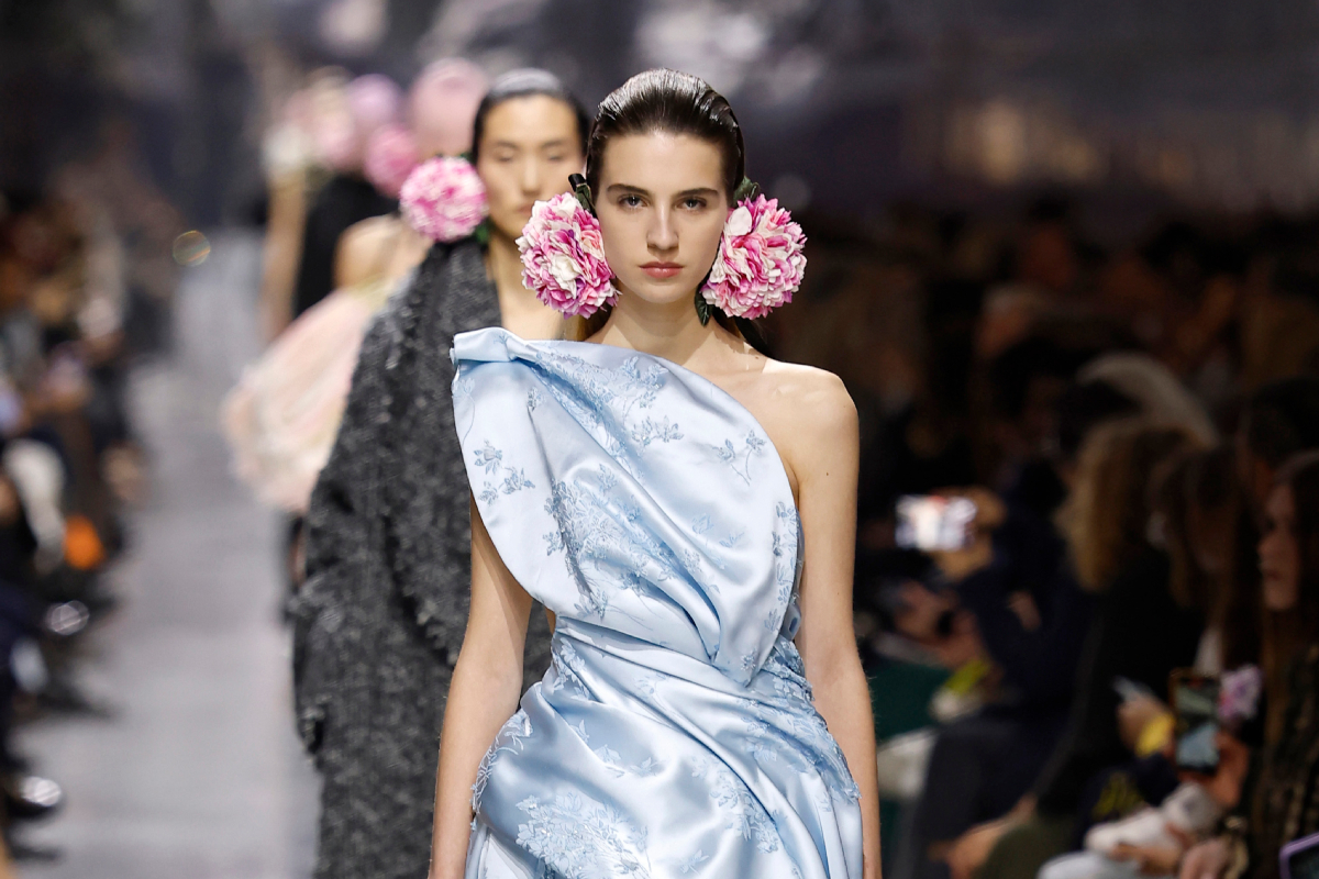 Barna hajú modell a Christian Dior 2026-os tavaszi–nyári haute couture bemutatóján világoskék estélyiben, virágos fülbevalóval