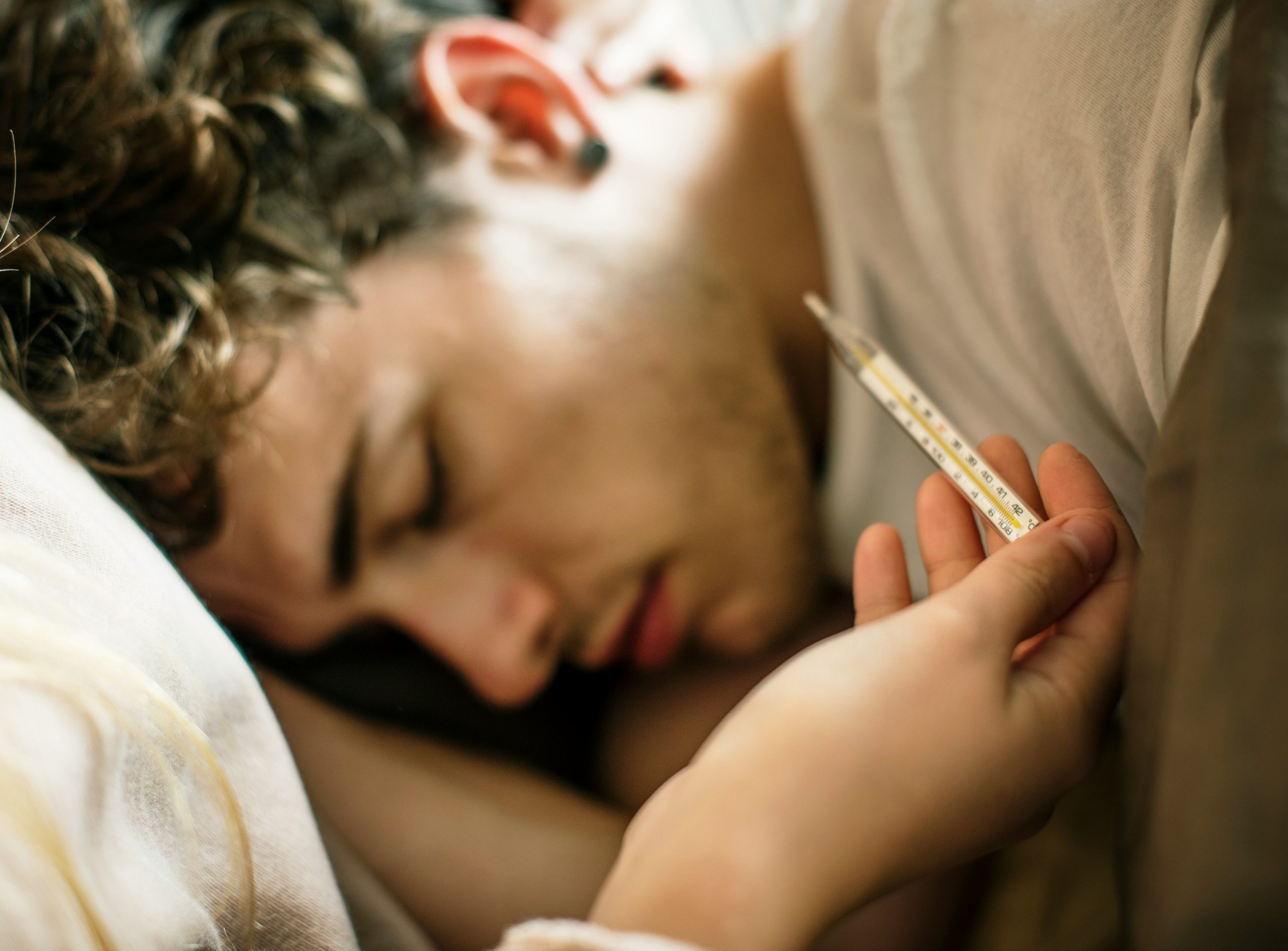 Fiatal férfi fáradtan és lázasan fekszik, az előtérben lázmérő