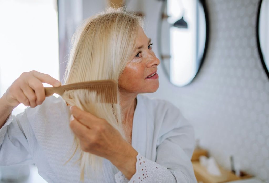 Idősebb szőke nő fa fésüvel húzza végig a haját
