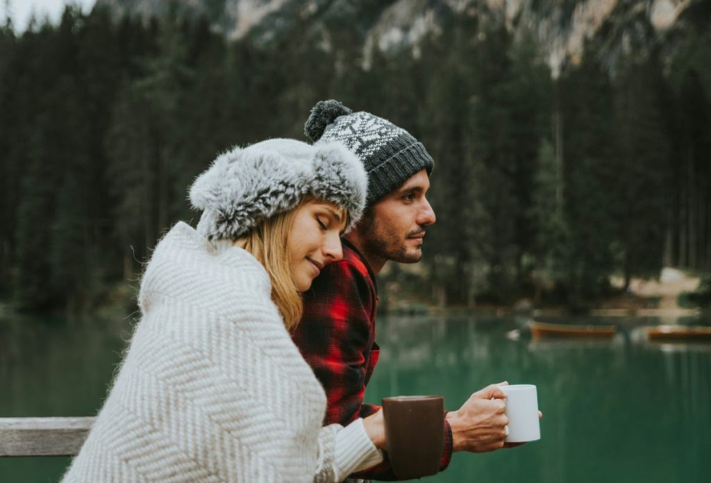 heti-horoszkop-2026-januar-26-februar-1-vizonto-szezon | Marie Claire Fiatal pár meghitt pillanatokat tölt el tóparton állva téli időhöz öltözködve sapkában, bögrét tartva a kezükben