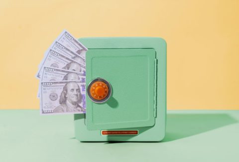 Sárga-mentazöld háttér, mentazöld miniszéf piros nyitóval, bankjegyek lógnak ki az ajtaján