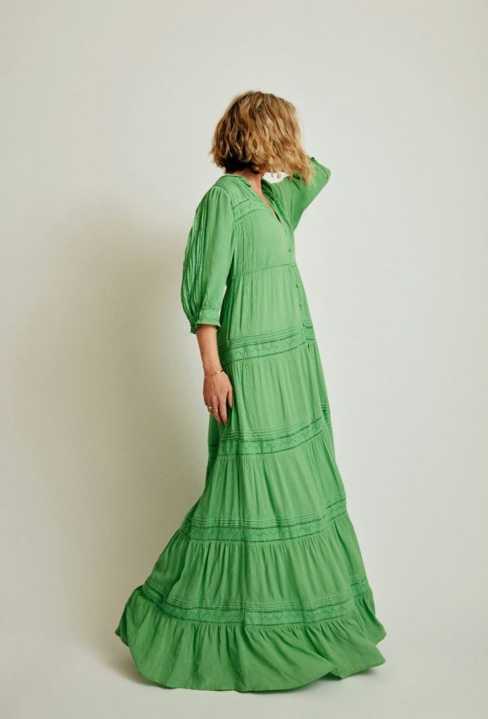 Szőke, bob frizurás nő elfordul a kamerától hosszú, lebegős zöld ruhában