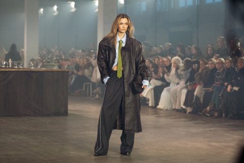 Szőke modell a Gestuz 2026-os őszi–téli bemutatóján bőr ballonkabátban, kék ingben, nyakkendőben, melegítőnadrágban