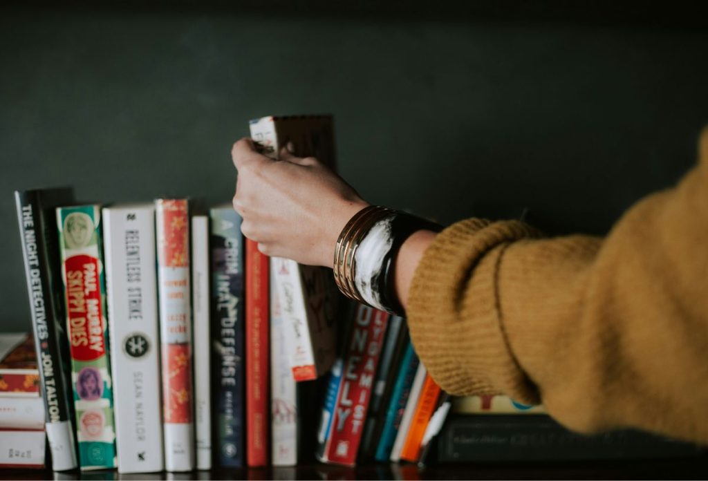 legjobb-hobbi-csendes-konyvklub | Marie Claire Nő mustársárga pulóverben könyvet tesz a polcra a többi közé