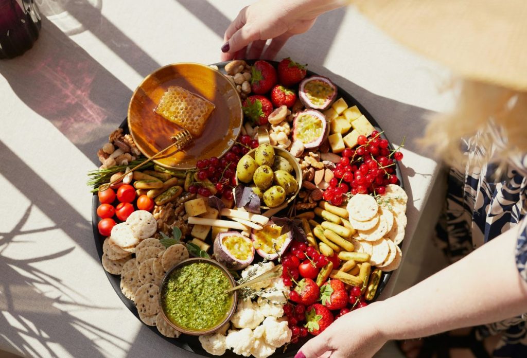 mediterran-etrend-gyulladascsokkento | Marie Claire Mediterrán étrend alapételek: magvak, olíva, gyümölcsök, zöldségek, méz nagy tálcán felülnézetből, amit egy nő tart