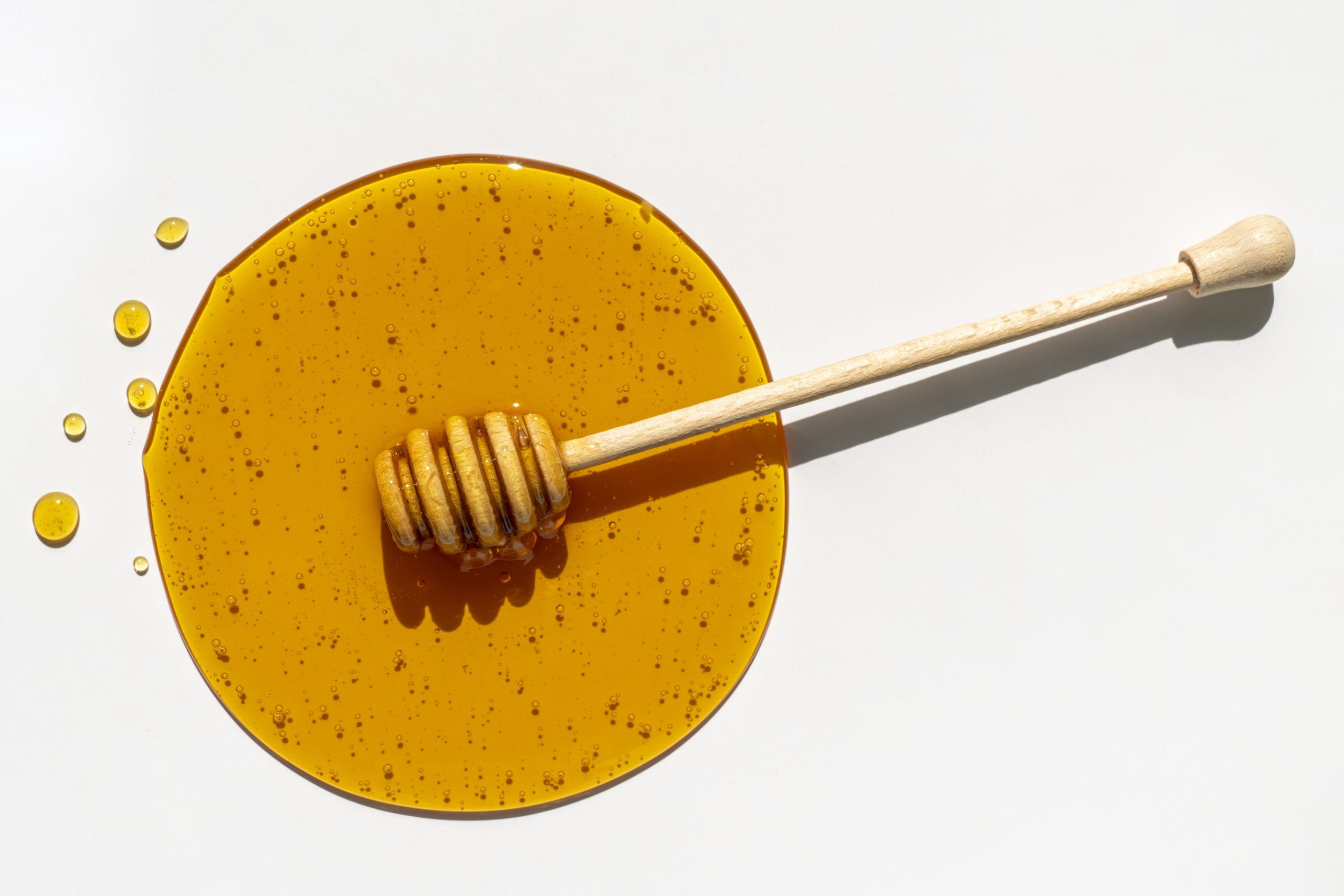 méz csepp és mézeskanál fejér háttéren