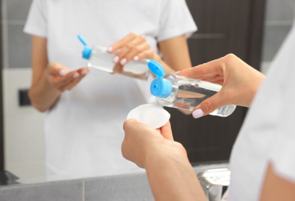 Micellás vizet tölt tükör előtt állva nő fehér pólóban fehér vattakorongra