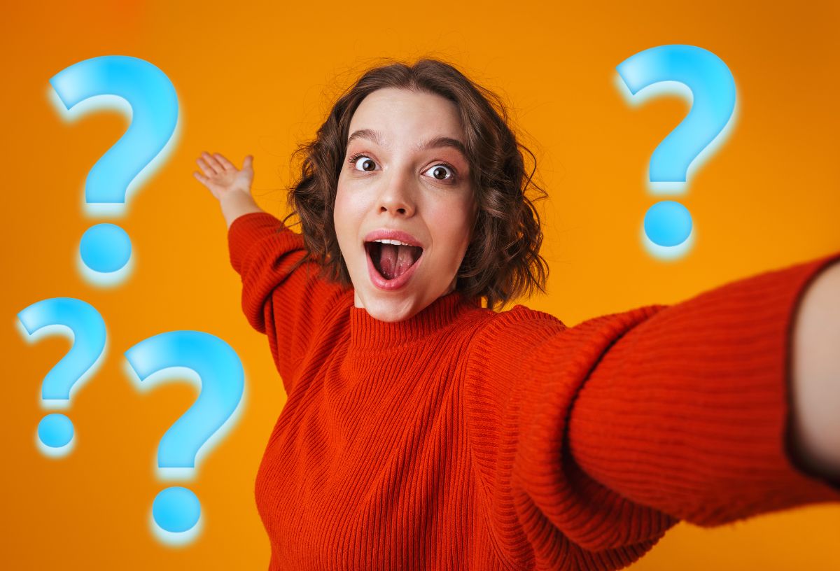 Narancszínű háttér előtt piros pulcsiban szelfiző fiatal lány csodálkozó arccal mutat maga mögé, kék kérdőjelek