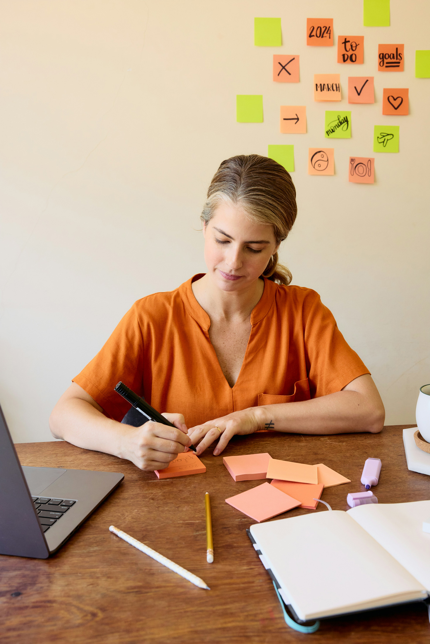 Egy nő papírra jegyzetel, előtte sok cetli és egy laptop látható