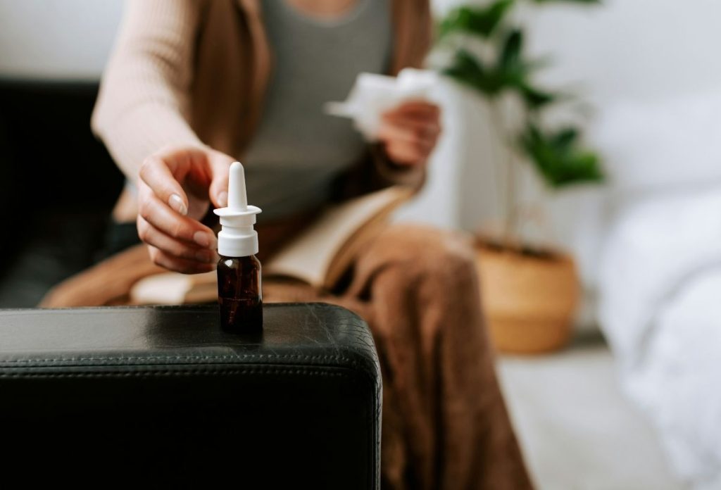 orr-orvosi-rejtely-orrspray | Marie Claire Orrspray után nyúl nő fekete kanapén, elmosódva látszik a háttérben, kezében papírzsebkendő