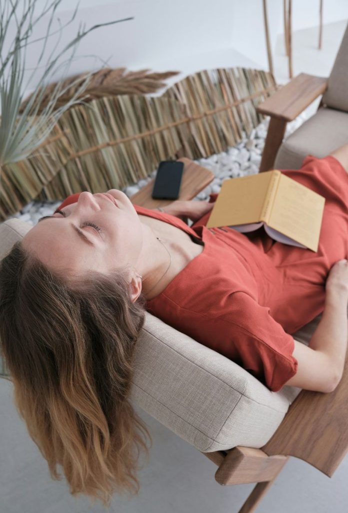 Nő piros ruhában kanapén fekve csukott szemmel pihen, az ölében sárga borítójú könyv