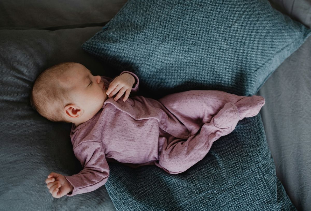 Újszülött kisbaba rózsaszín bodyban zöldeskék párnák között fekszik