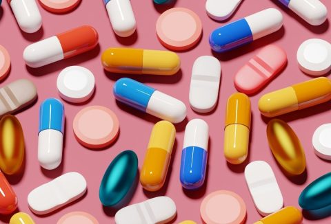 Változatos színű és méretű vitaminok, kapszulák és táplálékkiegészítők együtt rózsaszín háttéren