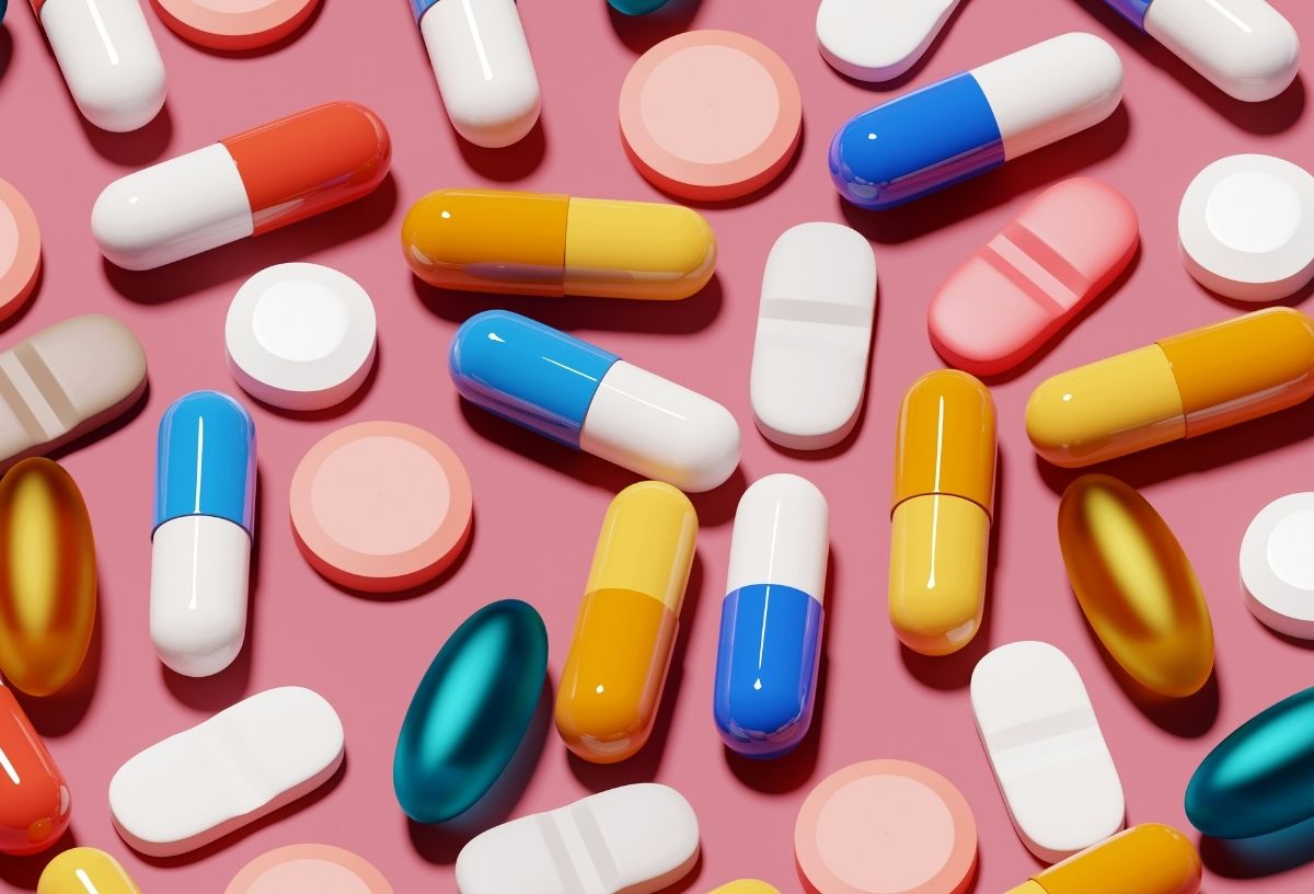 Változatos színű és méretű vitaminok, kapszulák és táplálékkiegészítők együtt rózsaszín háttéren