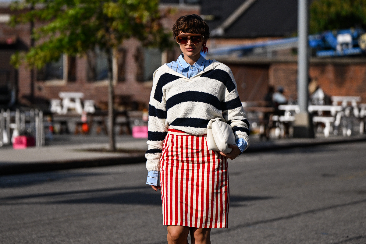napszemüveges modell kék ingben, rajta csíkos pulóver és piros fehér csíkos ceruzaszoknya